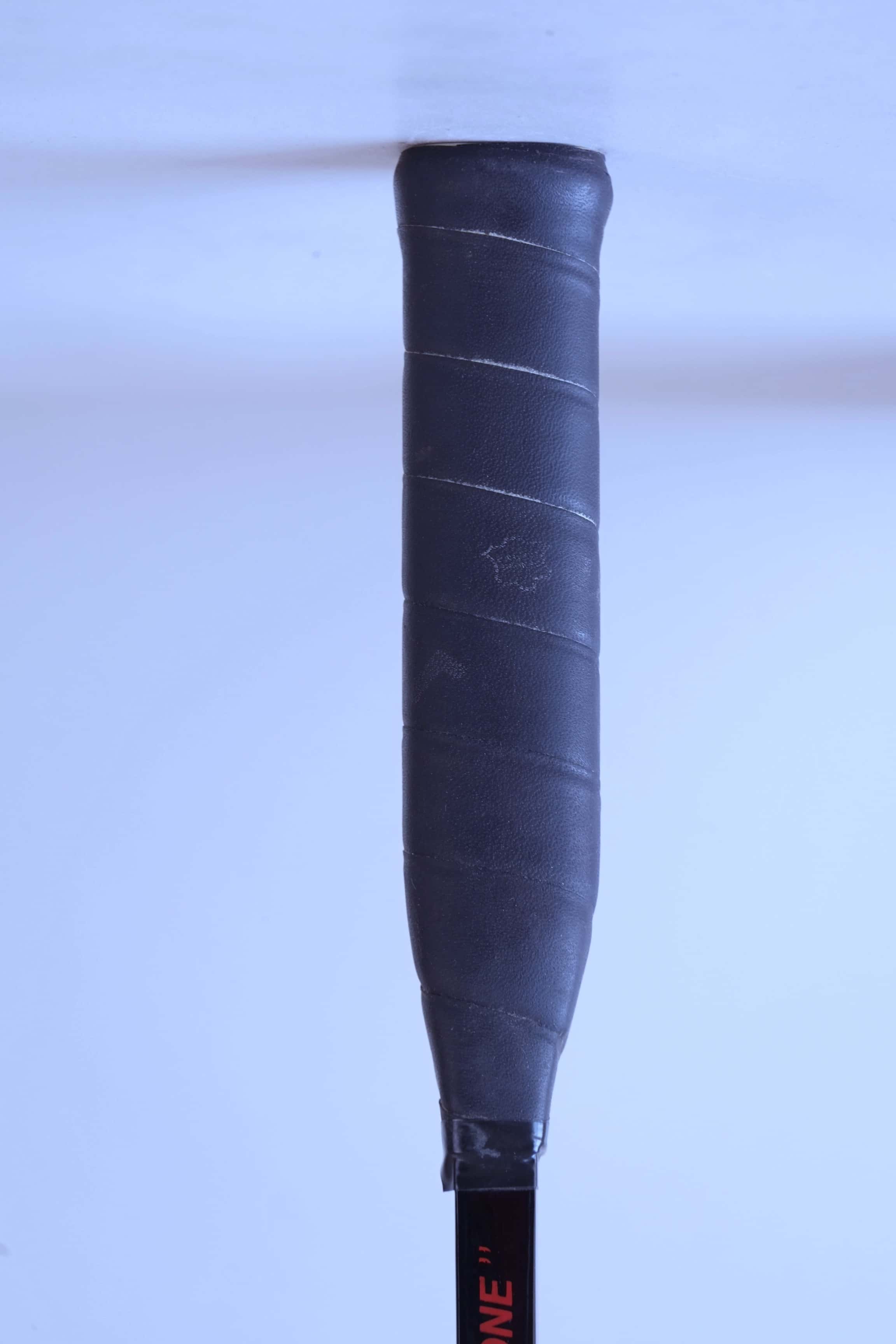 Close-up view of the original black textured leather wrap grip on a vintage squash racket handle.