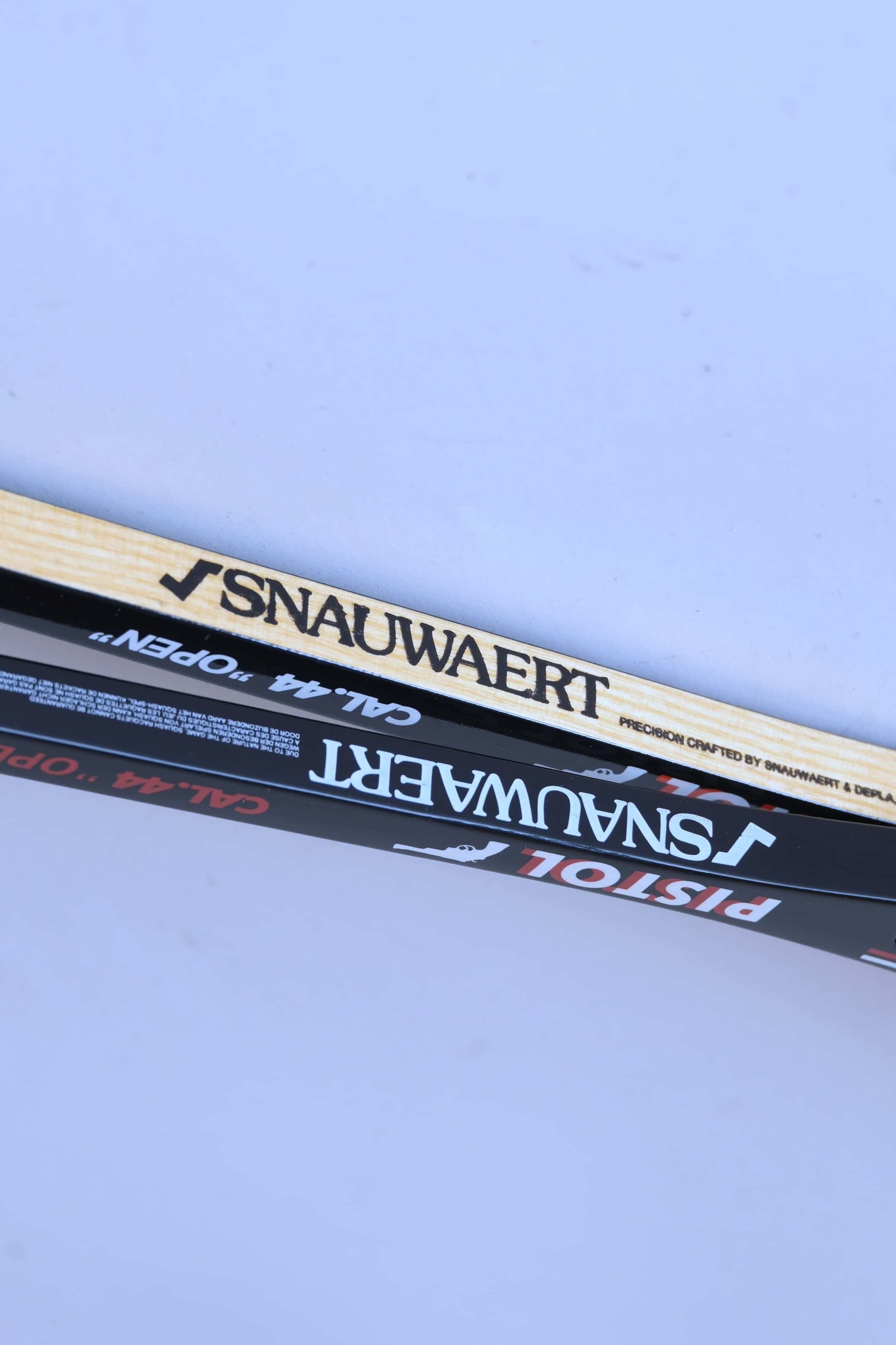Side-by-side comparison view of the shafts of a glossy black graphite racket and a natural wood grain racket, both displaying Snauwaert branding.