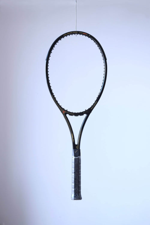 Studio full front shot of an unstrung black Snauwaert Royal Precision Ceramic tennis racquet with a grey grip and gold accents.