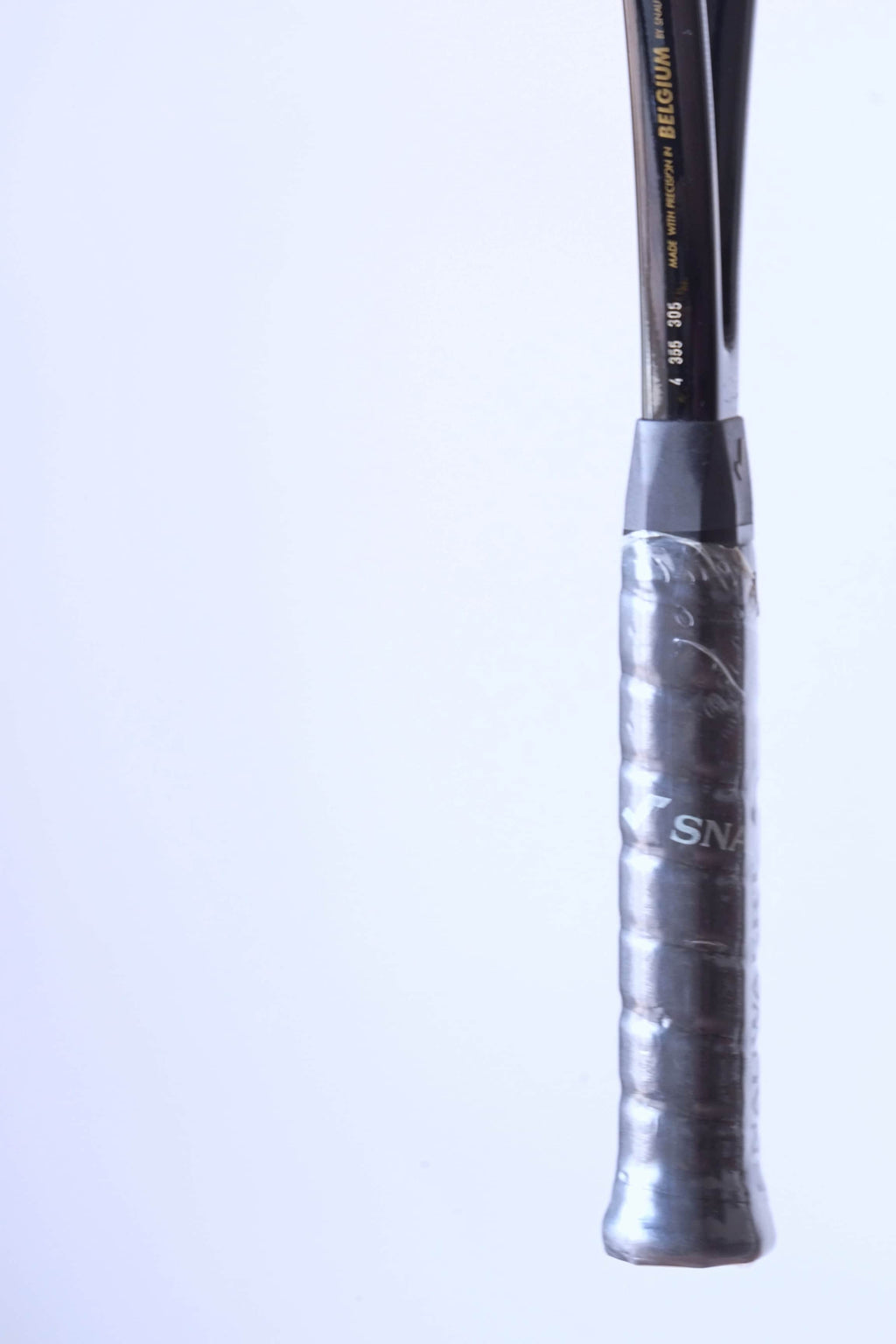 Close-up of the racquet shaft above the grip, showing the gold text "MADE WITH PRECISION IN BELGIUM BY SNAUWAERT" and serial numbers.
