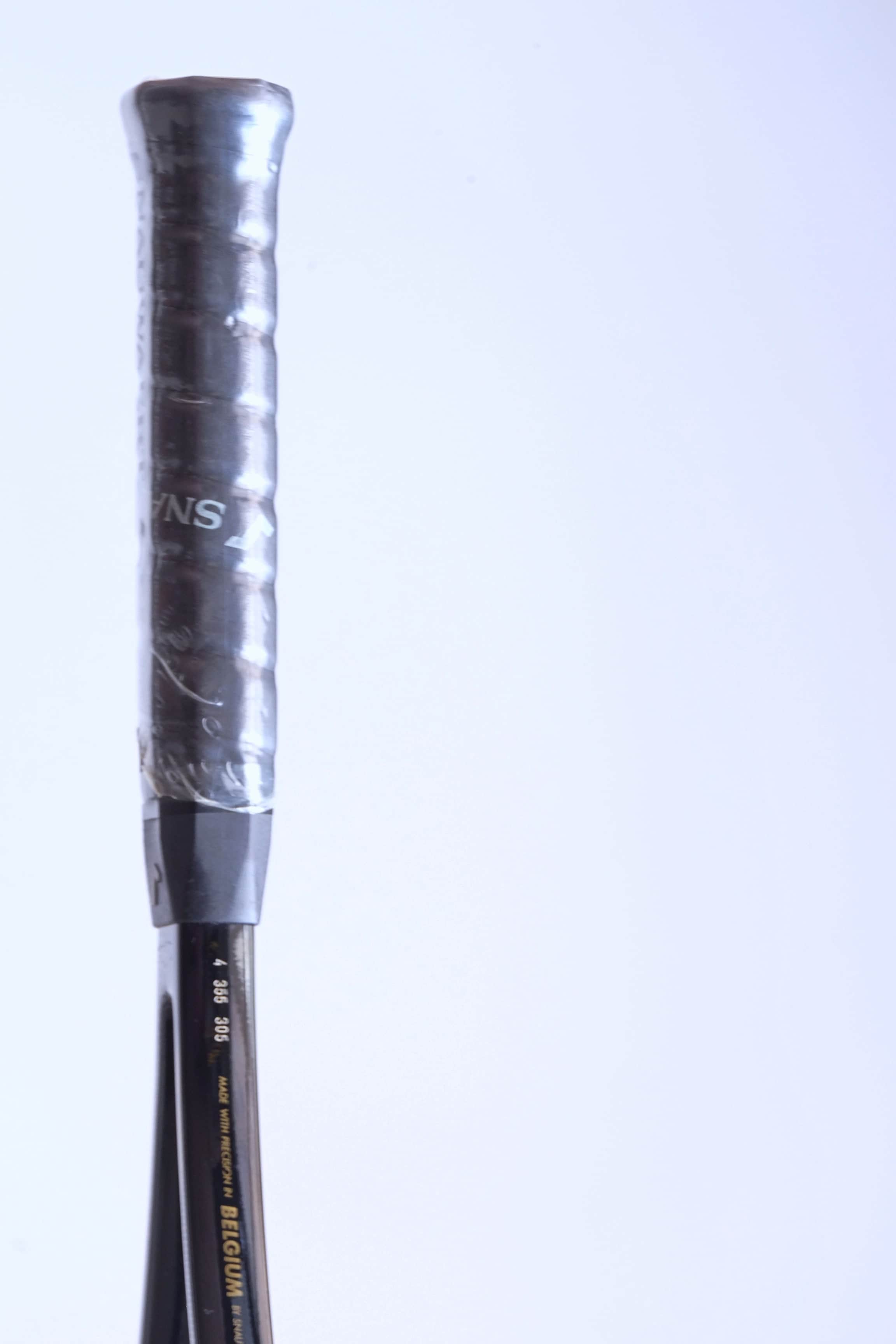 Close-up of the racquet shaft above the grip, showing the gold text "MADE WITH PRECISION IN BELGIUM BY SNAUWAERT" and serial numbers.
