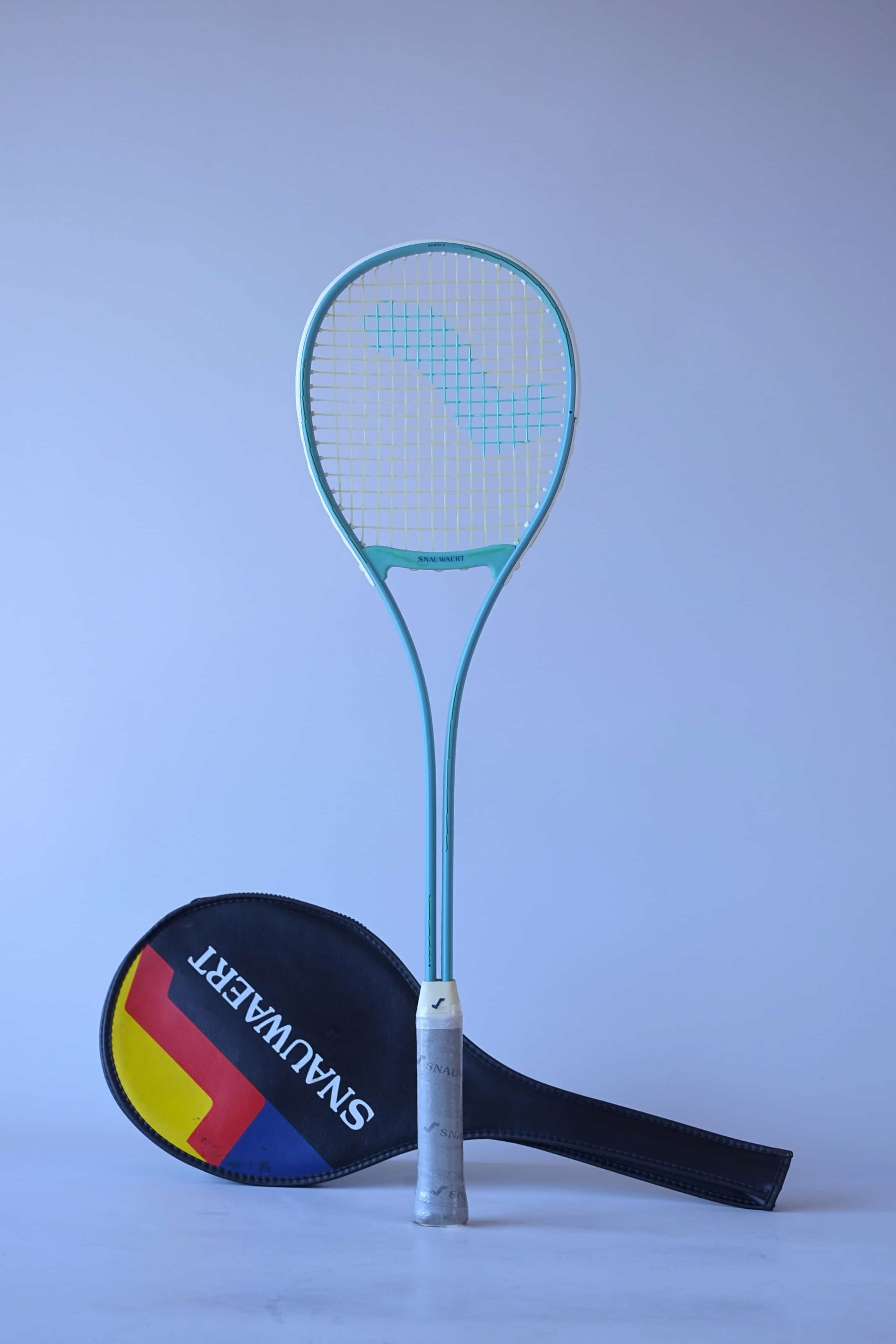 Snauwaert Shark 2 vintage squash racquet in teal standing upright alongside its original black Snauwaert shield cover with red, yellow and blue graphic.