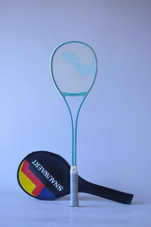 Snauwaert Shark 2 vintage squash racquet in teal standing upright alongside its original black Snauwaert shield cover with red, yellow and blue graphic.