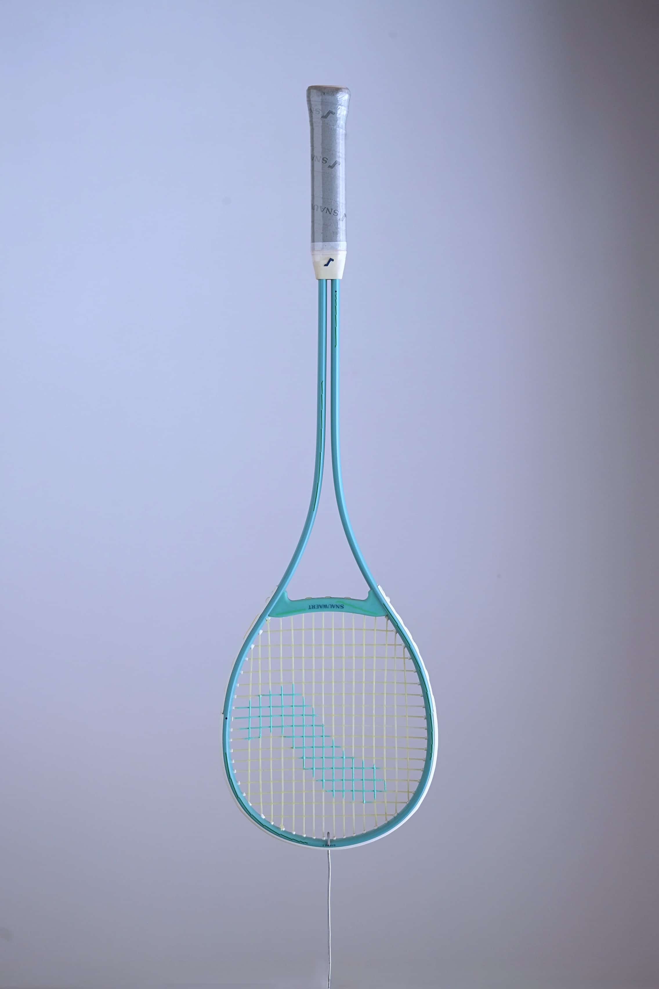 Snauwaert Shark 2 vintage squash racquet suspended against a light background, showing full teal frame, teardrop head and grey branded grip wrap.