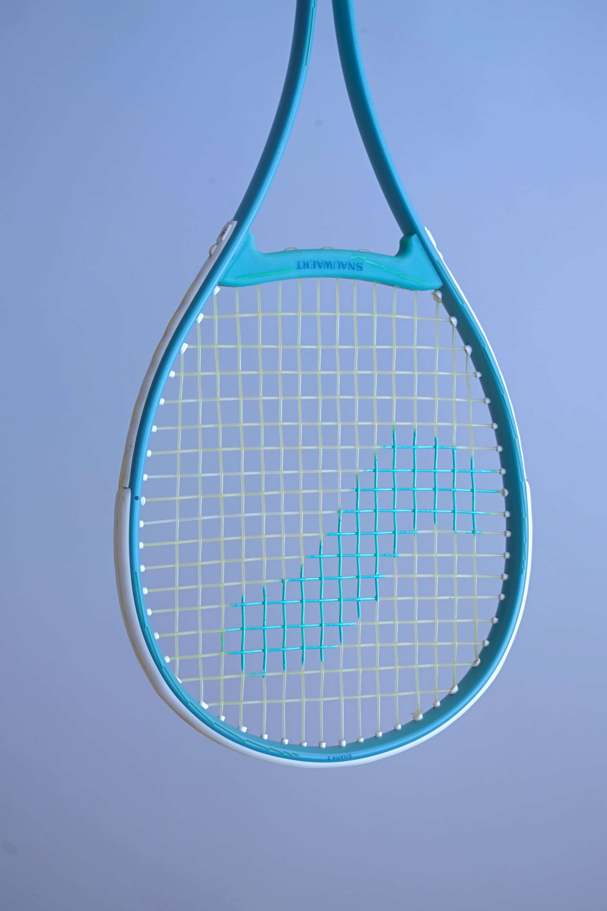 Angled front view of the Snauwaert Shark 2 squash racquet head showing teal and white frame, Snauwaert throat bridge and teal cross-string pattern on yellow-green mains.