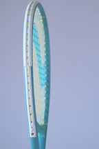 Side profile of the Snauwaert Shark 2 squash racquet head showing white bumper strip, teal frame and yellow-green string bed.