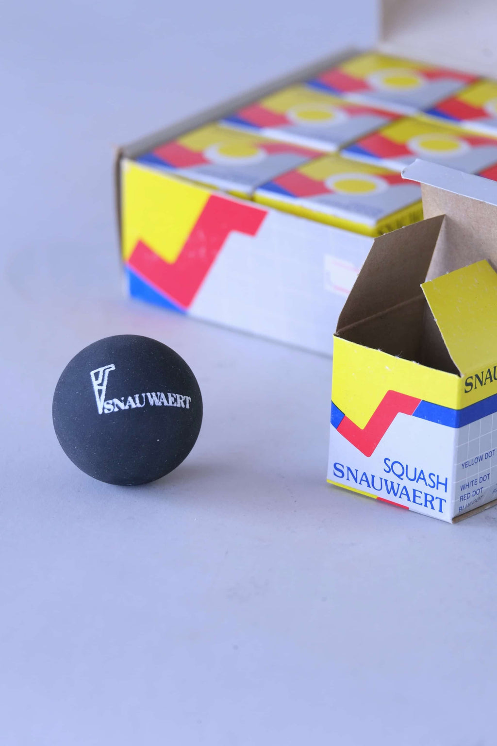 Close-up of a vintage black rubber squash ball featuring a printed Snauwaert logo.