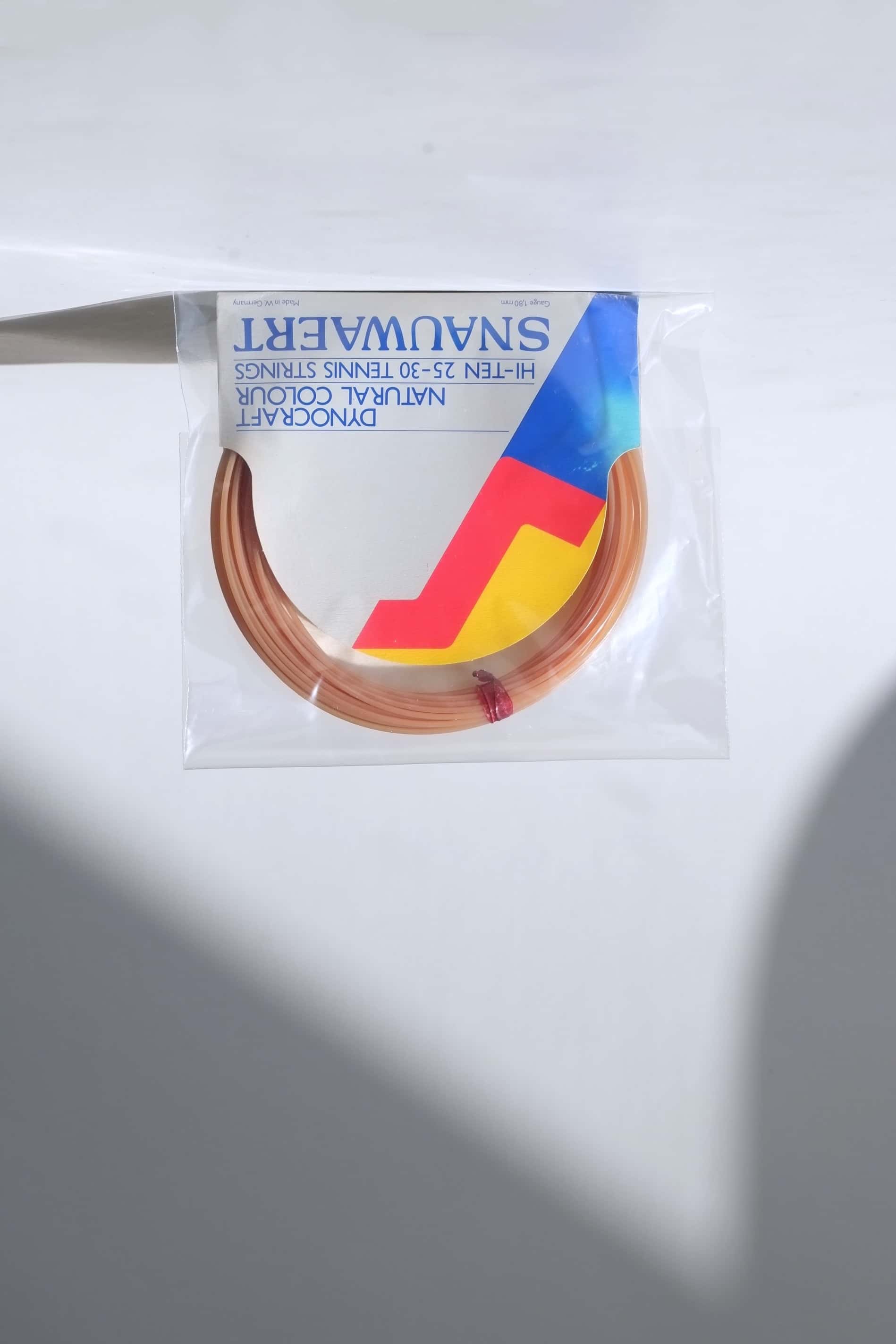 Deadstock vintage Snauwaert Dynocraft Hi-Ten 25-30 tennis strings in their original grey, yellow, and red and blue retail sleeve packaging.