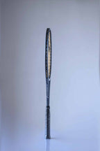 Side view of a vintage Snauwaert Hi-Ten25 tennis racquet. The frame is grey with the logo 'Snauwaert' printed in light grey, along the side. The racquet handle is black and wrapped in plastic.