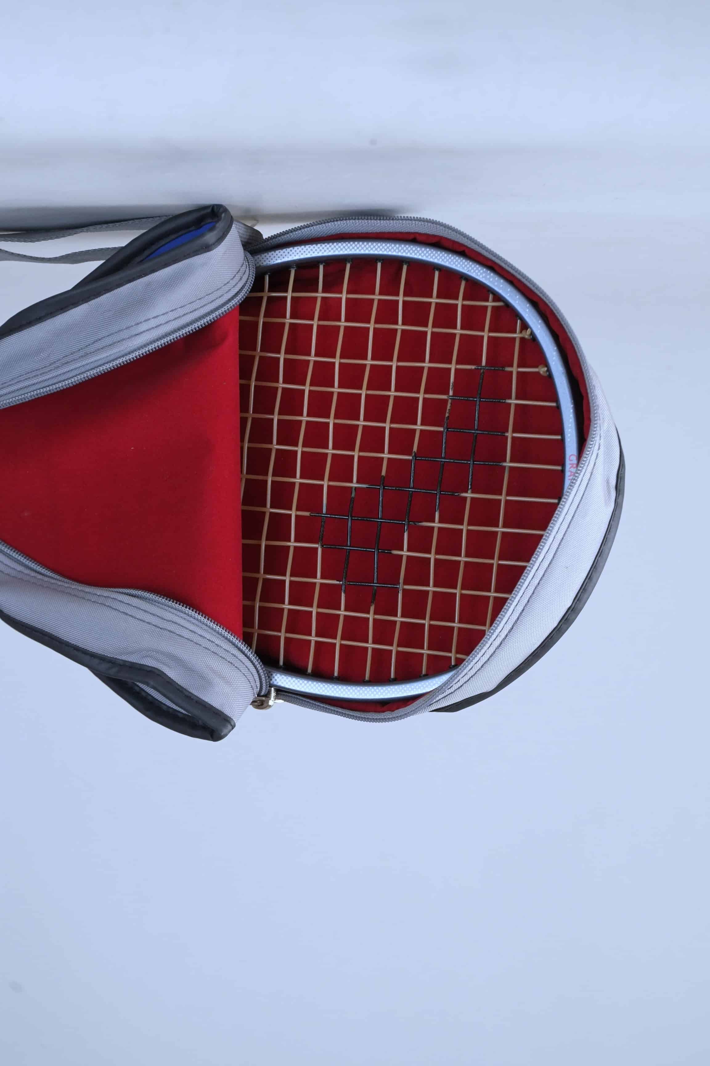 Inside view of the vintage Snauwaert racket bag, showcasing the red interior lining and zipper construction, with a racket inside.