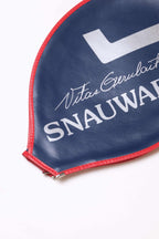 Close-up shot of the white printed Vitas Gerulaitis script signature and Snauwaert block text on a navy blue grained vinyl racquet cover with red stitched edges.