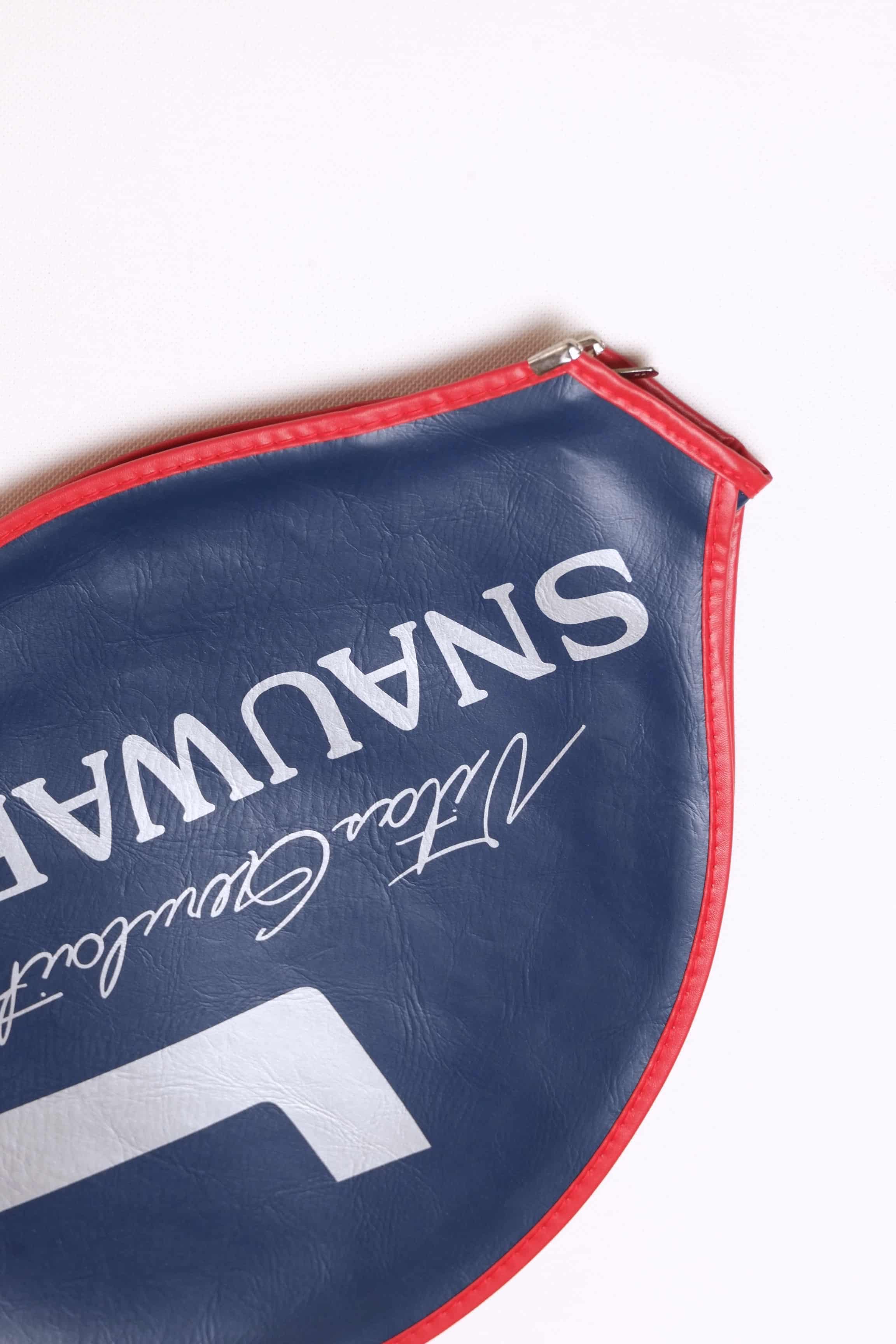 Close-up shot of the white printed Vitas Gerulaitis script signature and Snauwaert block text on a navy blue grained vinyl racquet cover with red stitched edges.