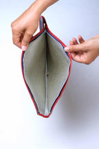Hands holding open a vintage Snauwaert racquet cover to reveal its textured grey-green interior lining and silver-toothed zipper track with red vinyl trim.