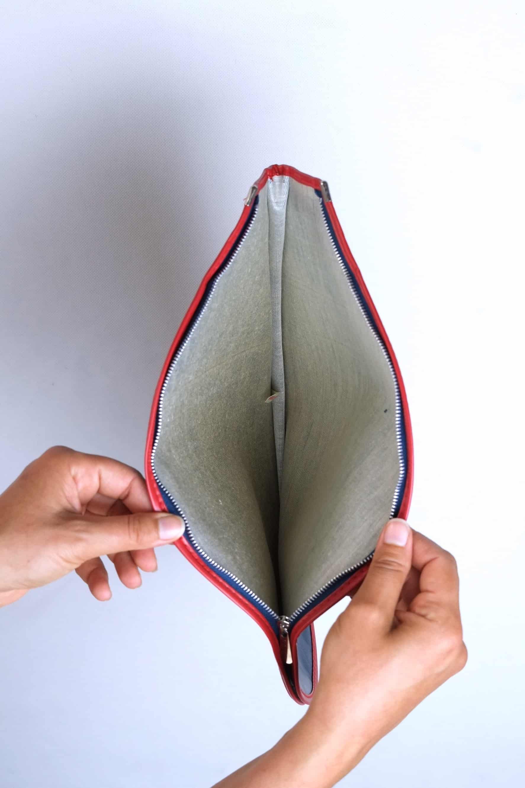 Hands holding open a vintage Snauwaert racquet cover to reveal its textured grey-green interior lining and silver-toothed zipper track with red vinyl trim.