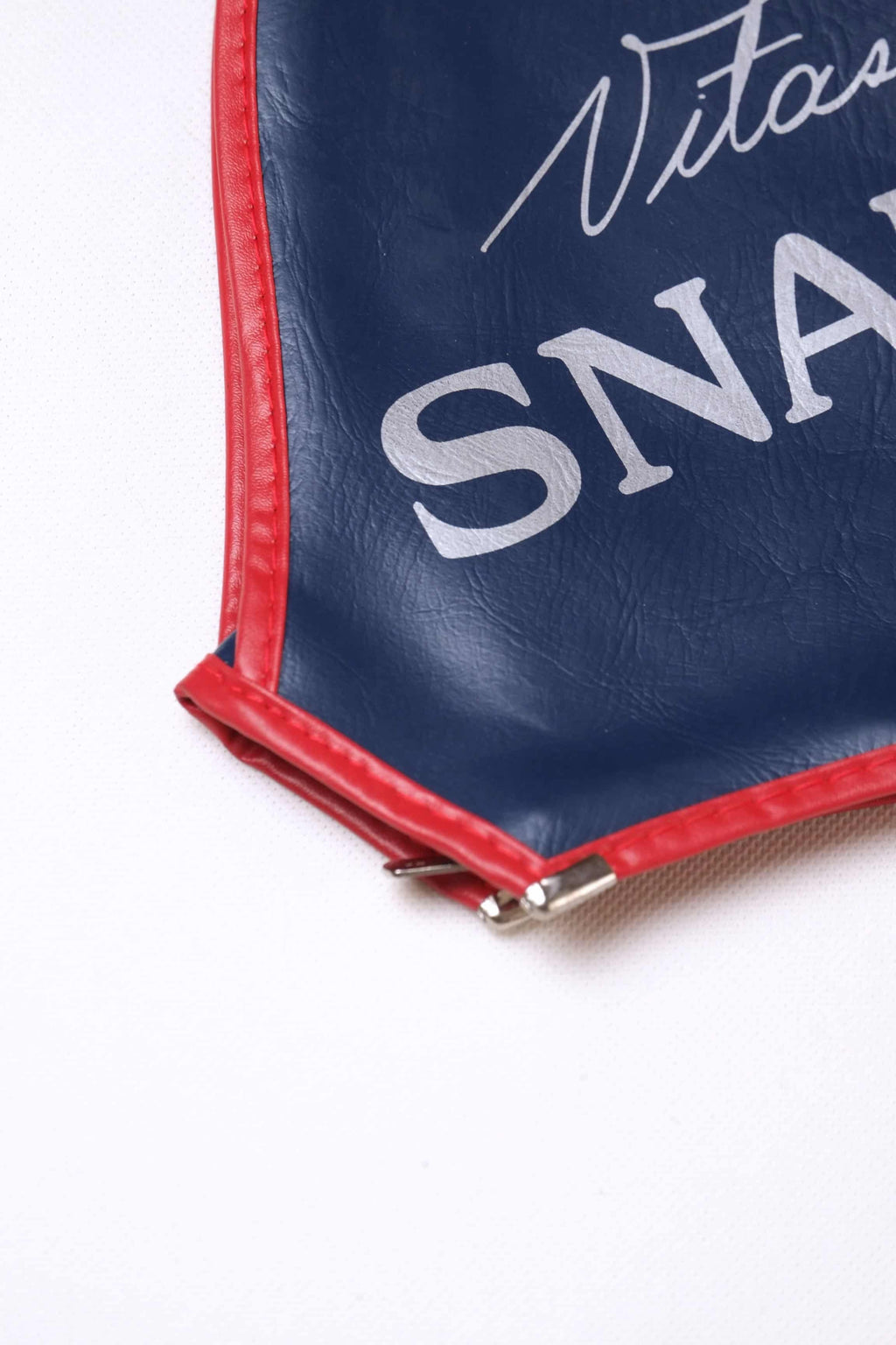 Detailed macro shot of the metal zipper base and crisp red piping on a vintage navy blue vinyl Snauwaert tennis racquet cover.