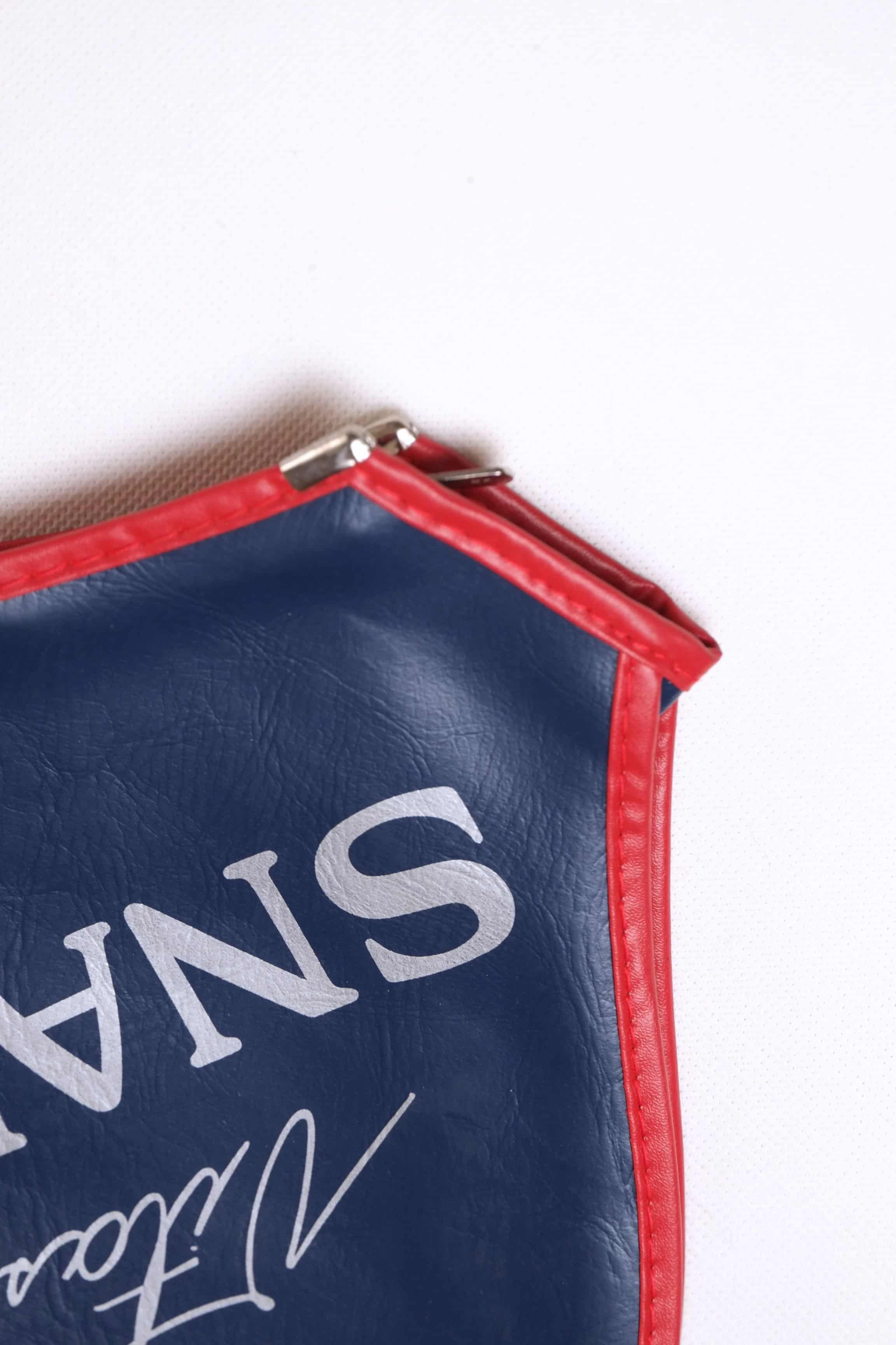 Detailed macro shot of the metal zipper base and crisp red piping on a vintage navy blue vinyl Snauwaert tennis racquet cover.