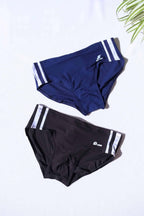 Two pairs of vintage SOLAR 70s swim briefs in navy and black with white double stripe detailing and printed logo, laid flat on white background.