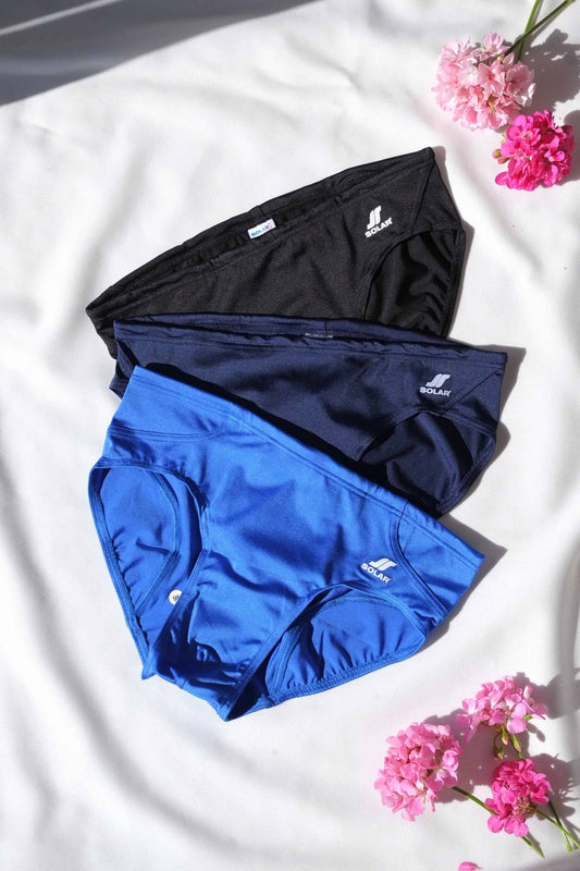 Three SOLAR vintage 70s swim briefs in black, navy, and bright royal blue, laid out under natural light.