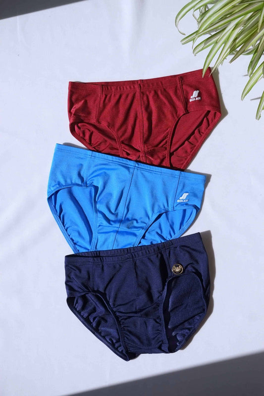 Three SOLAR vintage 70s swim briefs in burgundy red, blue, and navy laid flat under bright lighting.