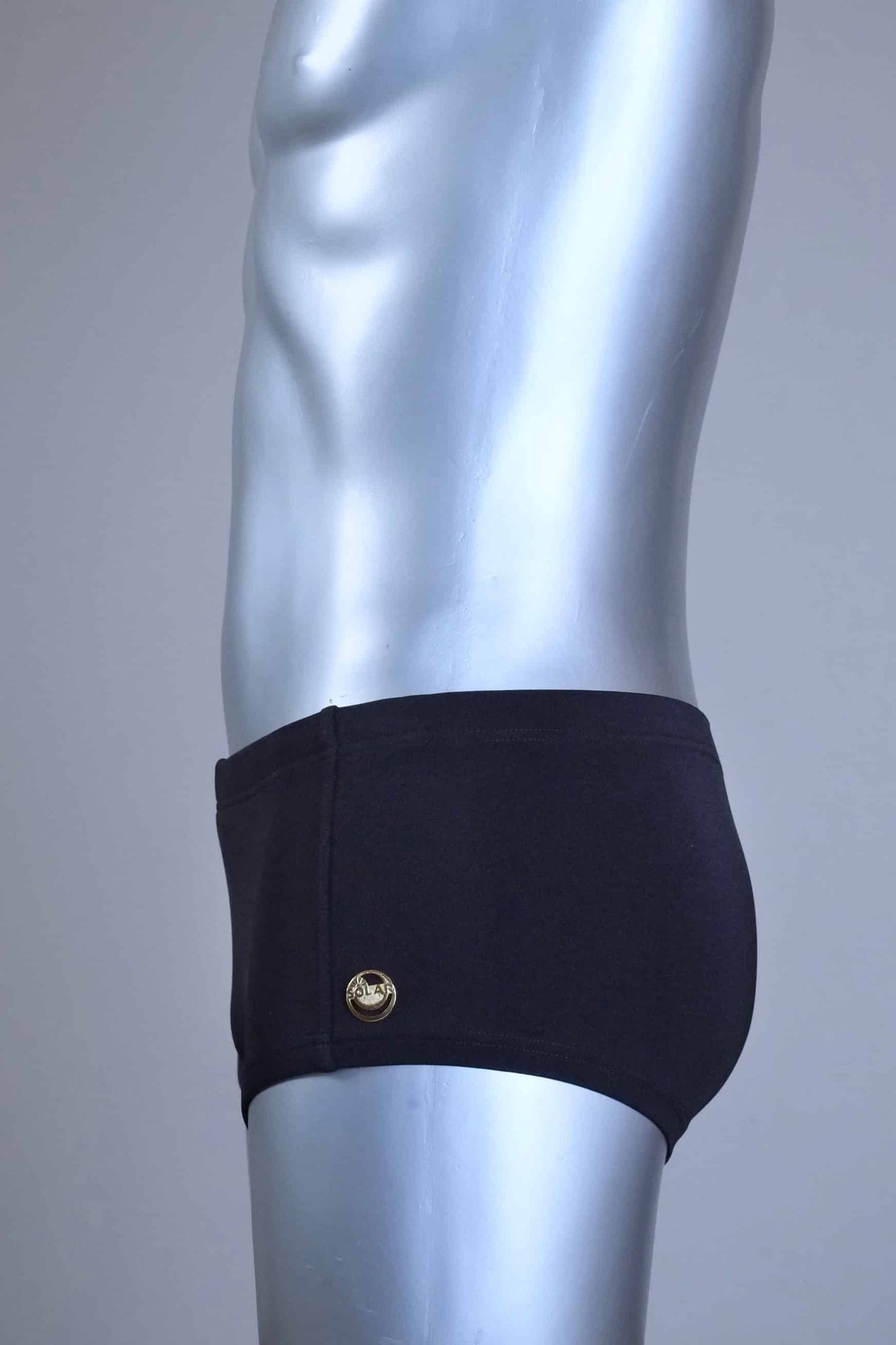 Side view of a Mannequin wearing a pair of vintage 70s SOLAR swim trunks in black against a grey background.