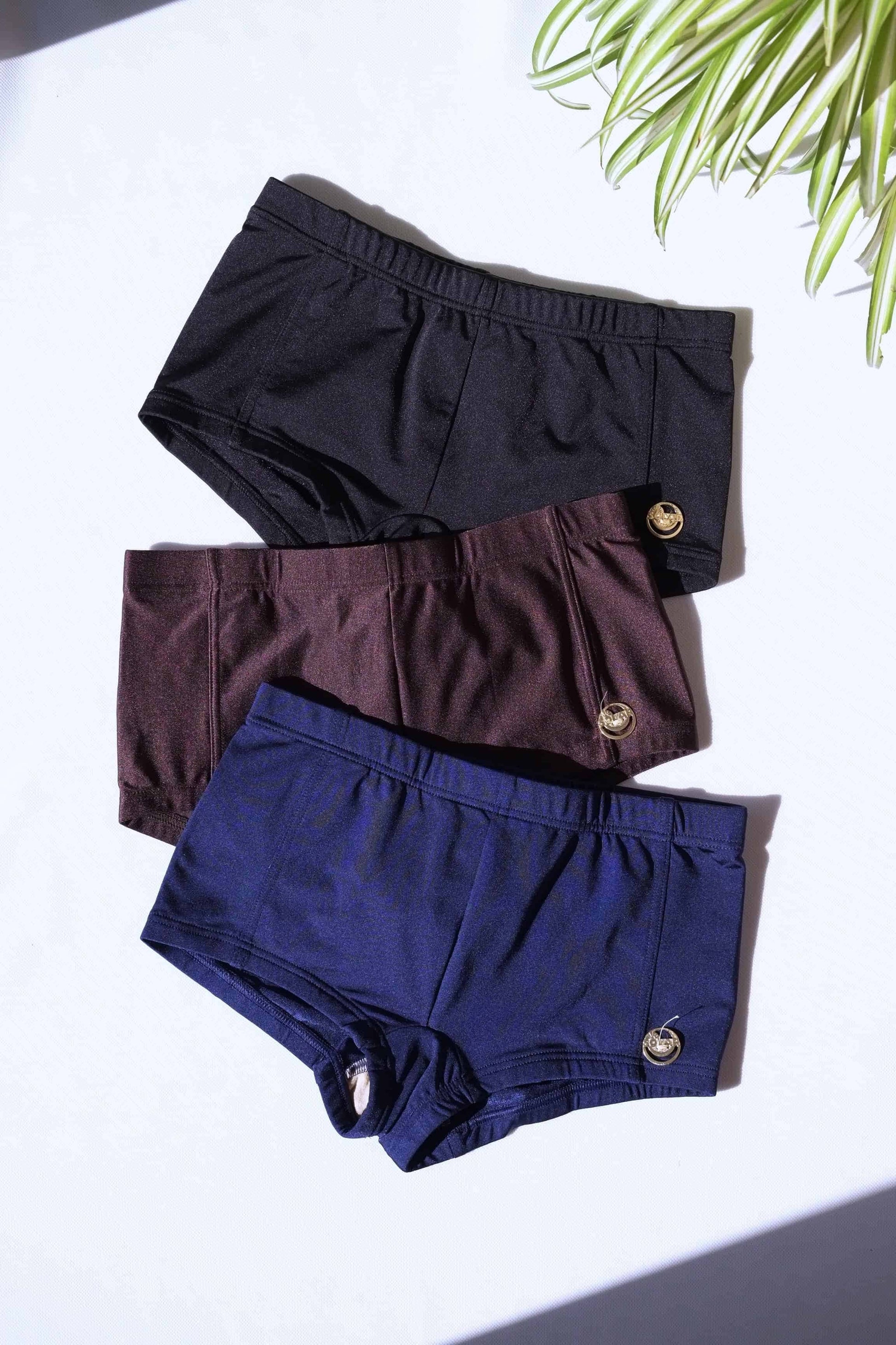 Set of three vintage 70s SOLAR swim trunks in black, brown, and navy with gold metal logo badge on each.