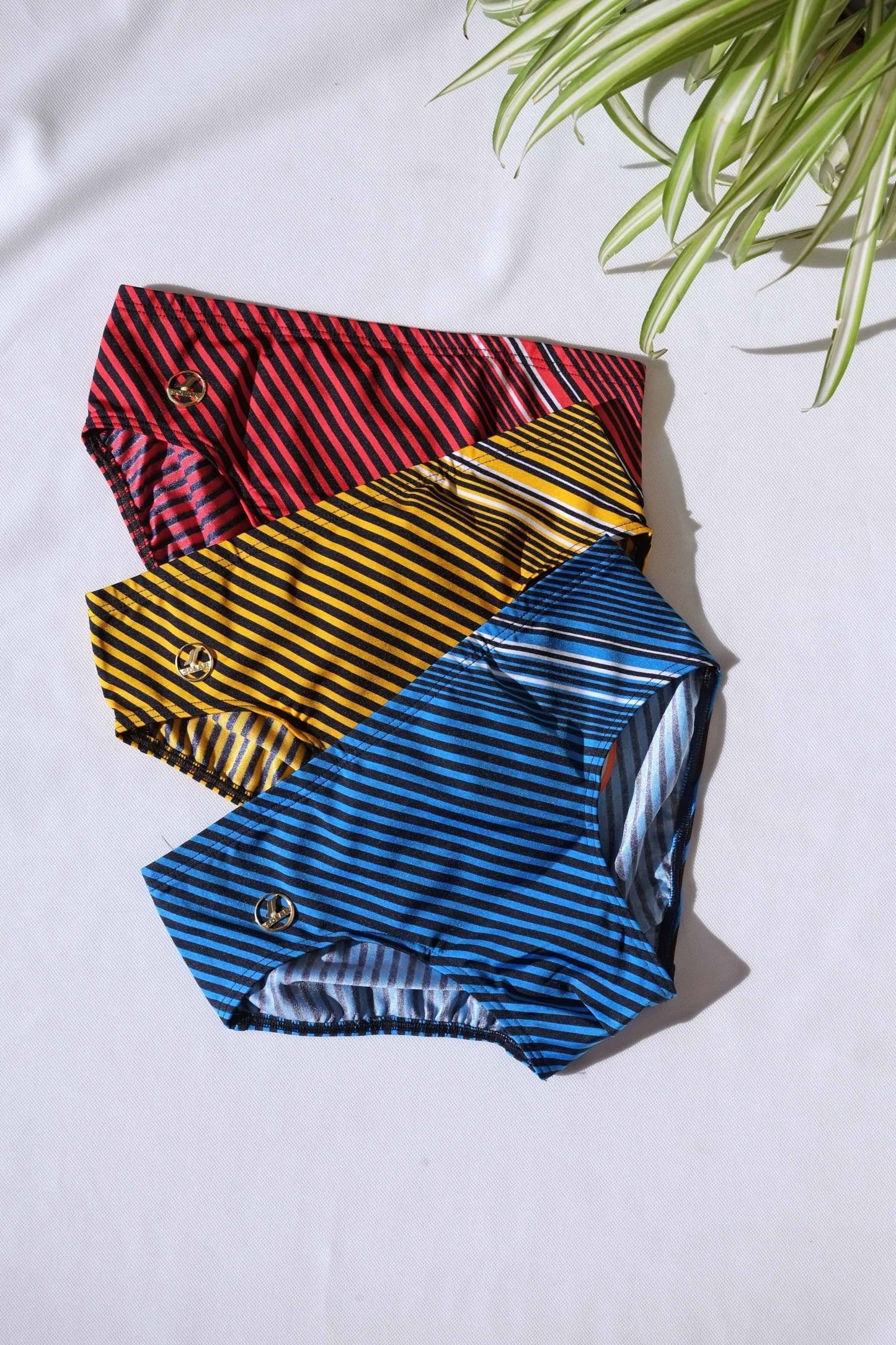 Three pairs of SOLAR brand vintage 80s men's swim briefs with horizontal and angled stripes in red, yellow, and blue, aid flat on a white background.