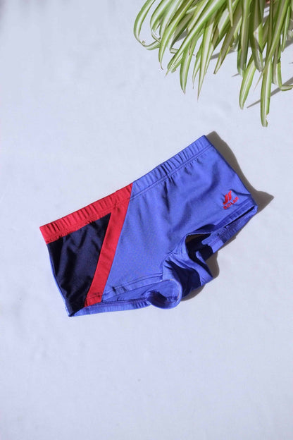 A single pair of SOLAR brand vintage 80s men's square-cut swim briefs in purple with a red and black diagonal color block.
