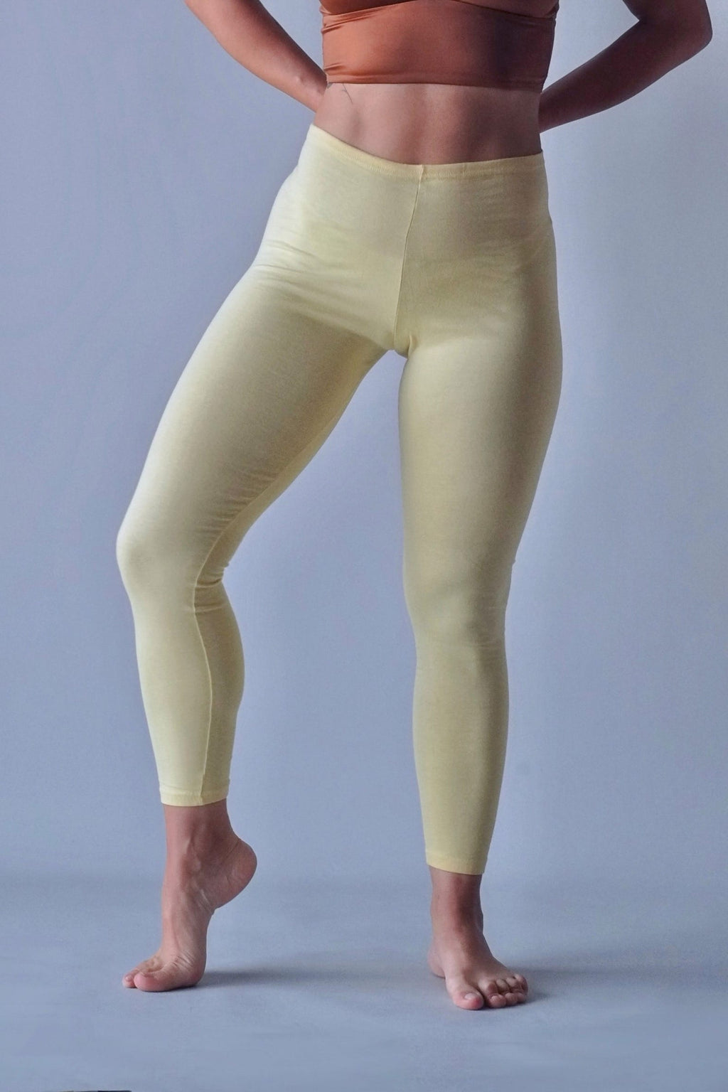 Solar vintage 80s solid cotton leggings in pale yellow worn on a female model — wide high-rise waistband, slim full-length cut, dynamic standing pose, front view