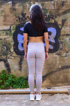 Solar vintage 80s micro stripe cotton leggings worn on a female model — fine pink and blue stripes on heather grey base, slim full-length cut, styled with white sneakers, rear view against urban wall backdrop