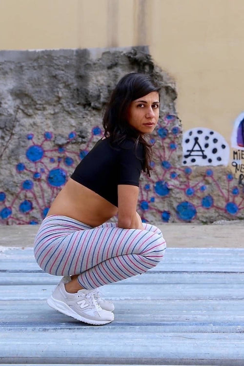 Solar vintage 80s micro stripe cotton leggings worn on a female model — fine pink and blue stripes on heather grey base, slim full-length cut, squatting pose, styled with New Balance sneakers, side view
