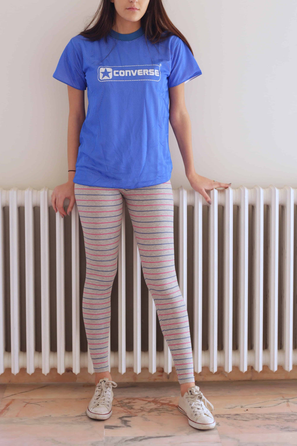 Solar vintage 80s micro stripe cotton leggings worn on a female model — fine pink and blue stripes on heather grey base, slim full-length cut, styled with white Converse sneakers and blue Converse t-shirt, relaxed standing pose, front view