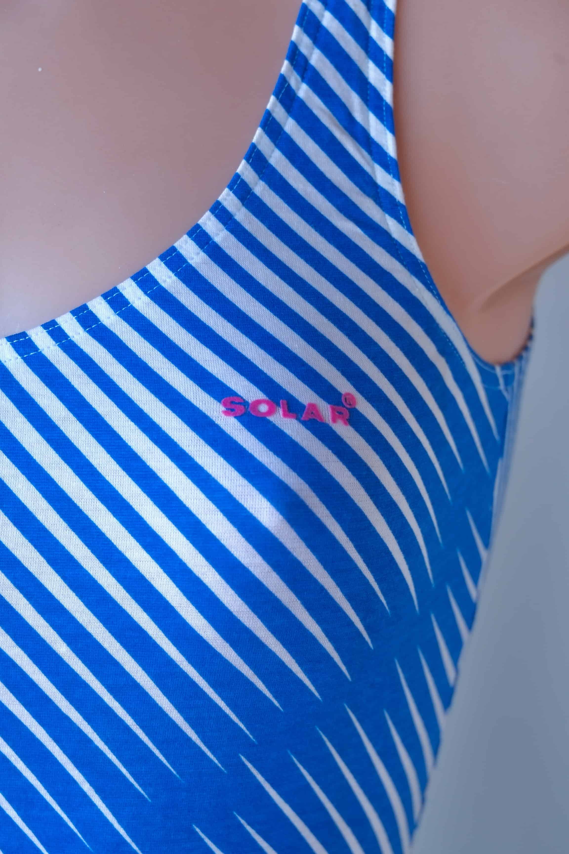 Close view of a blue and white diagonal striped Solar leotard with tank-style straps, showing the pink printed logo Solar.