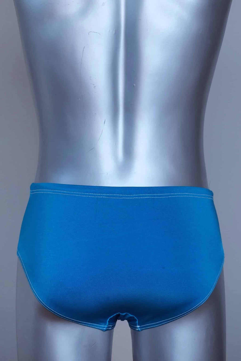 Back view of a vintage turquoise men's swim briefs on a silver mannequin against a gray background