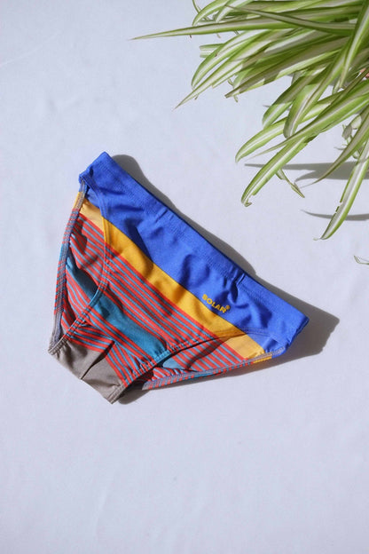 A pair of SOLAR brand vintage 80s men's swim briefs with multi-colored horizontal stripes in blue, yellow, and red hues, laid flat on a white background.