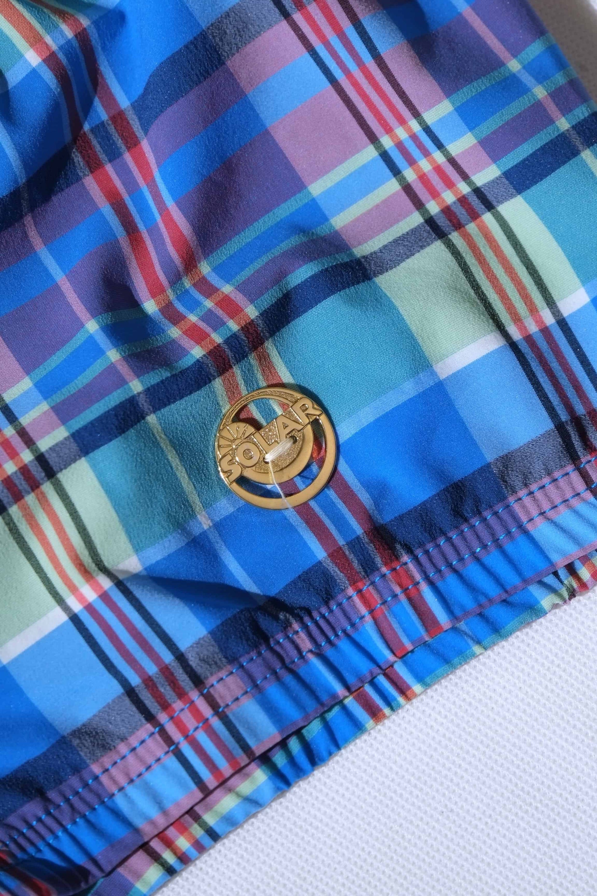 Close up of Back view of A vintage pair of Blue plaid swim briefs showing a gold logo badge