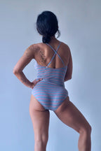 Solar vintage 80s pinstripe spaghetti strap leotard worn on a female model — heather grey with fine pink and blue pinstripes, cross-back spaghetti straps, high cut leg, dynamic standing pose, rear view