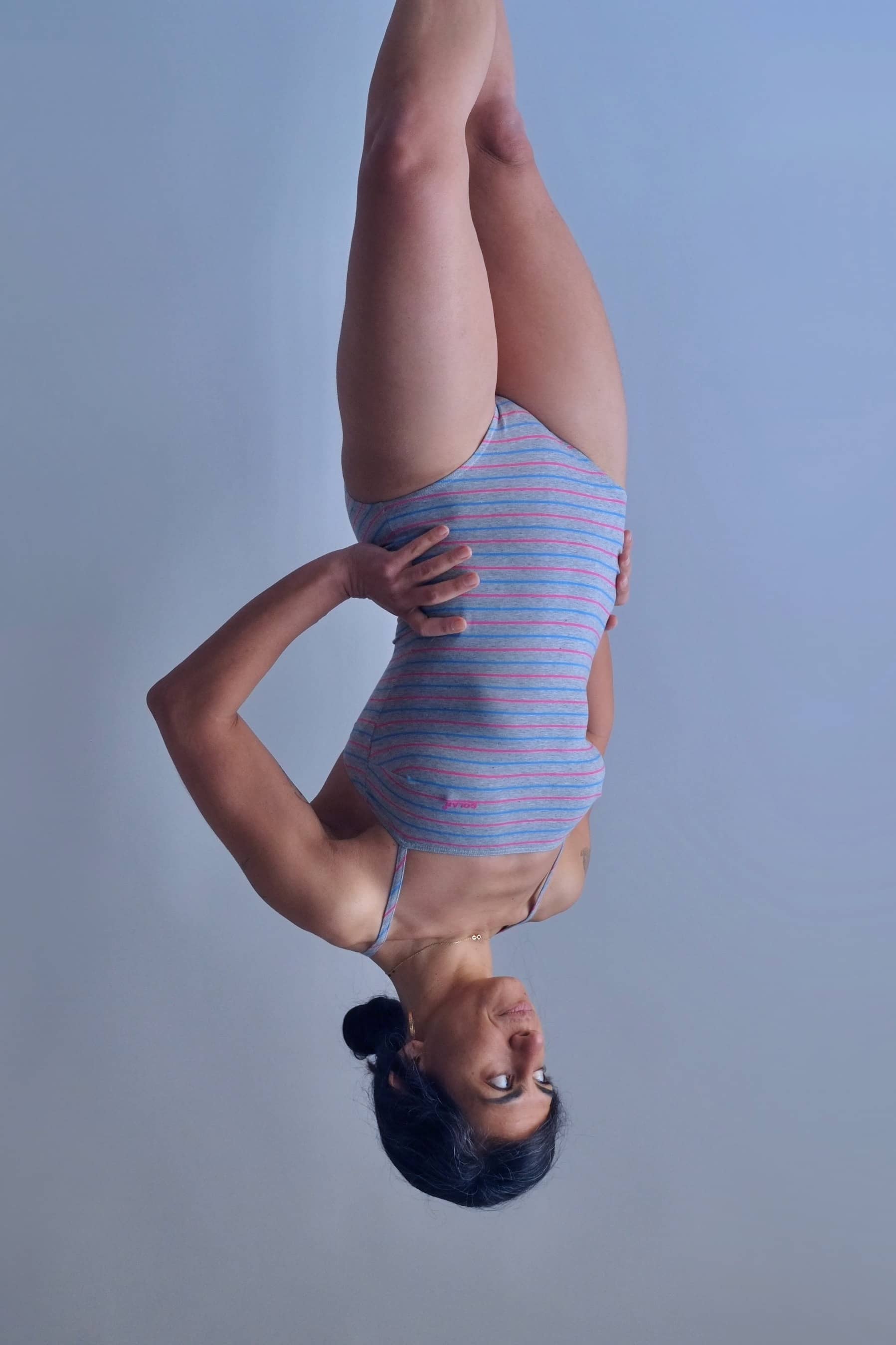 Solar vintage 80s pinstripe spaghetti strap leotard worn on a female model — heather grey with fine pink and blue pinstripes, straight bandeau neckline, spaghetti straps, high cut leg, three-quarter standing pose, front view