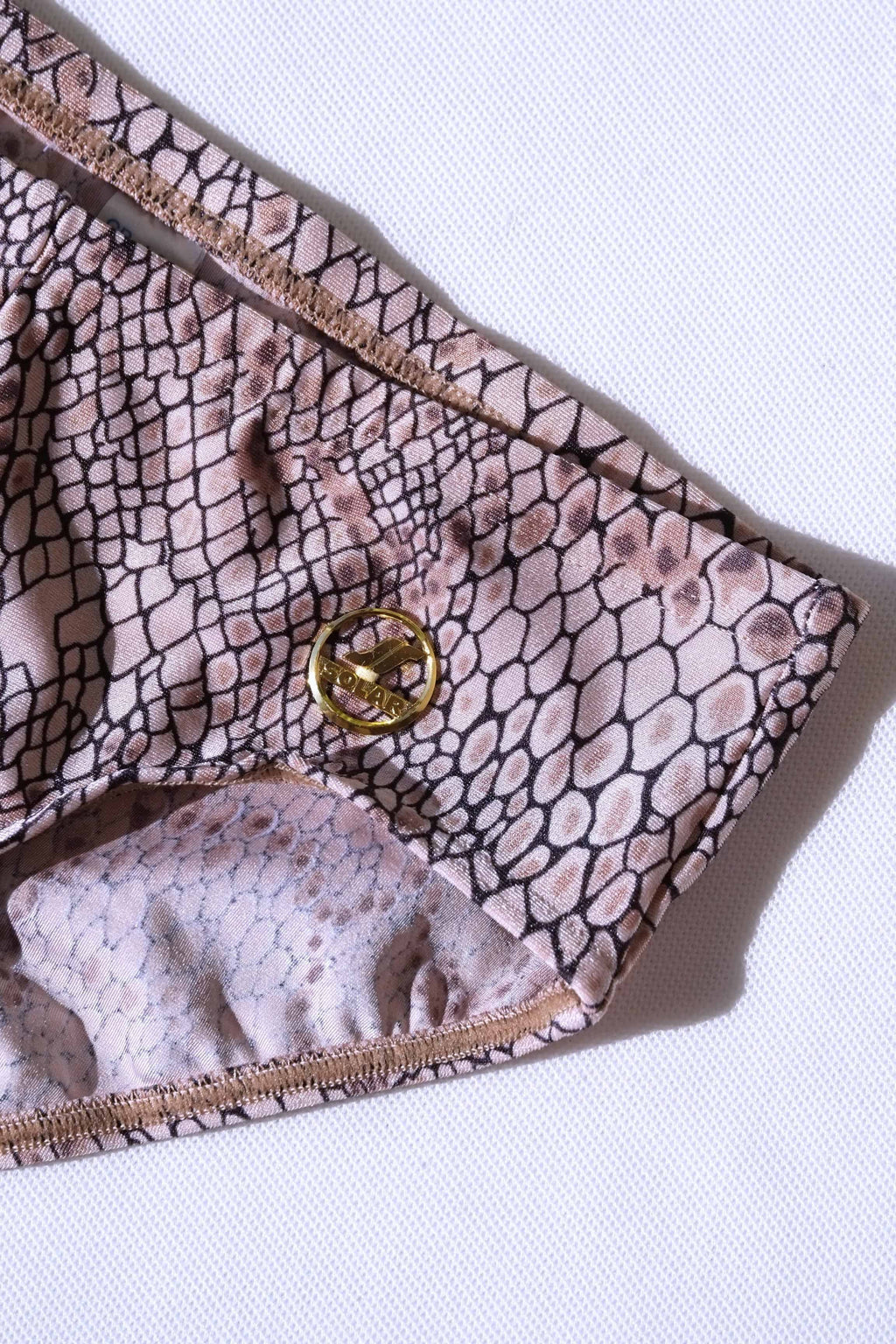 Close up of a pair of SOLAR brand vintage 80s men's swim briefs with a light brown snakeskin print and a gold metal logo.