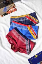 Three pairs of colorful swim shorts on a white background with magazines in the background.
