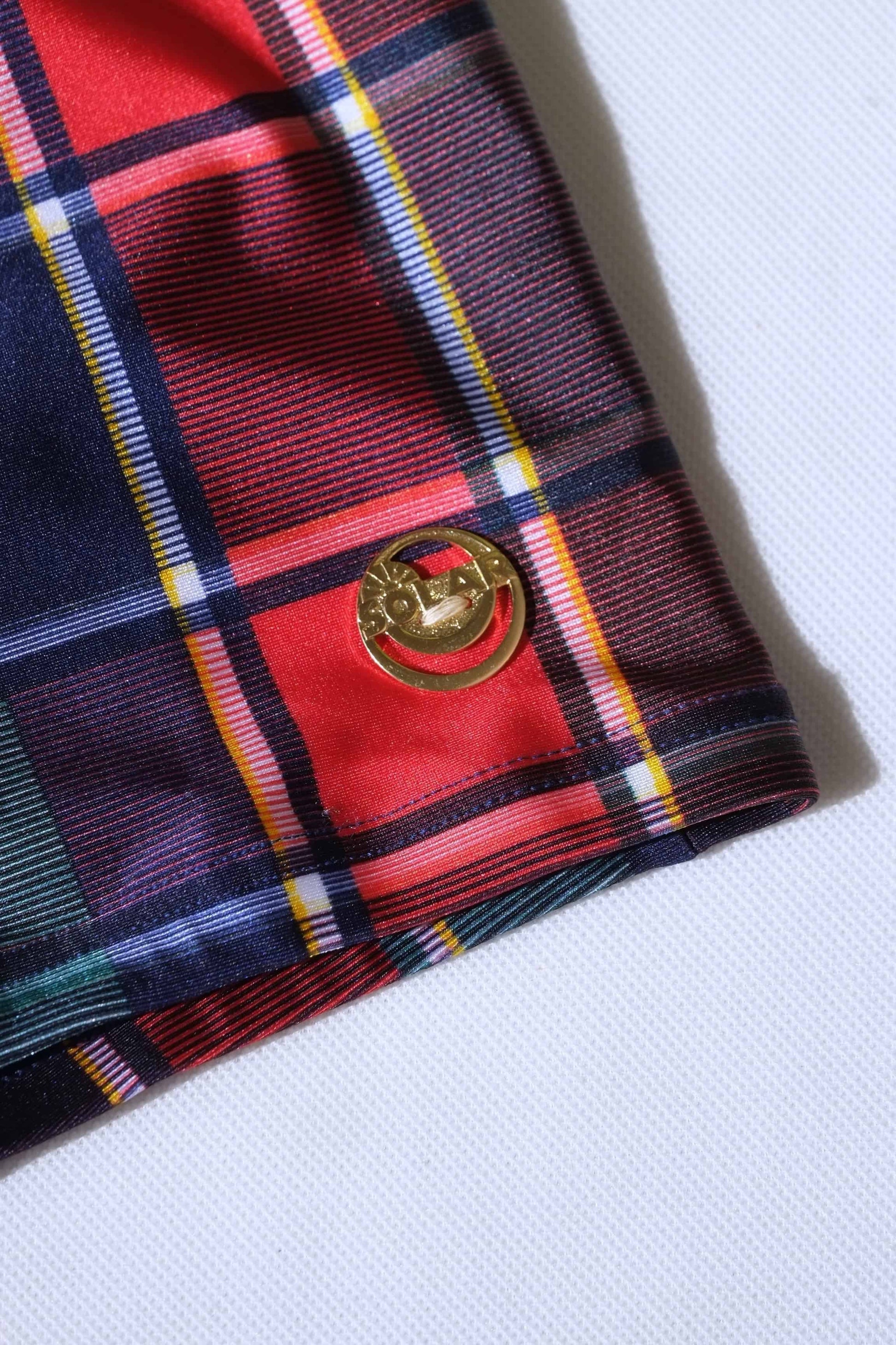 Closeup of a vintage plaid swim briefs with a gold logo badge on a white background
