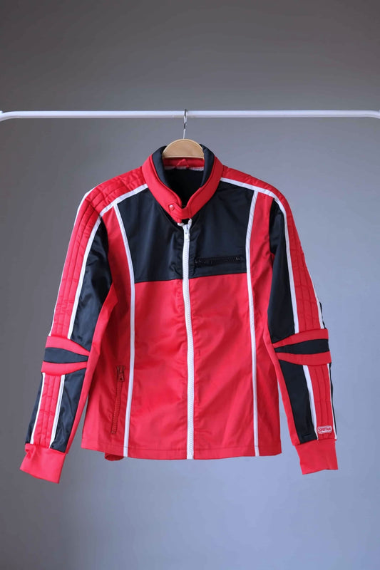 Front view of a vintage Sportalm ski jacket. The jacket is predominantly red with black panels and white piping. It features padded shoulders and elbows, a stand-up collar, and a zipper closure.