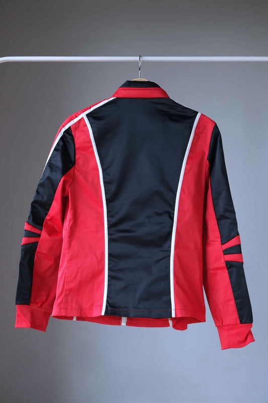 Back view of a vintage Sportalm ski jacket. The jacket is predominantly red with black panels and white piping. It features padded shoulders and elbows, a stand-up collar, and a zipper closure.