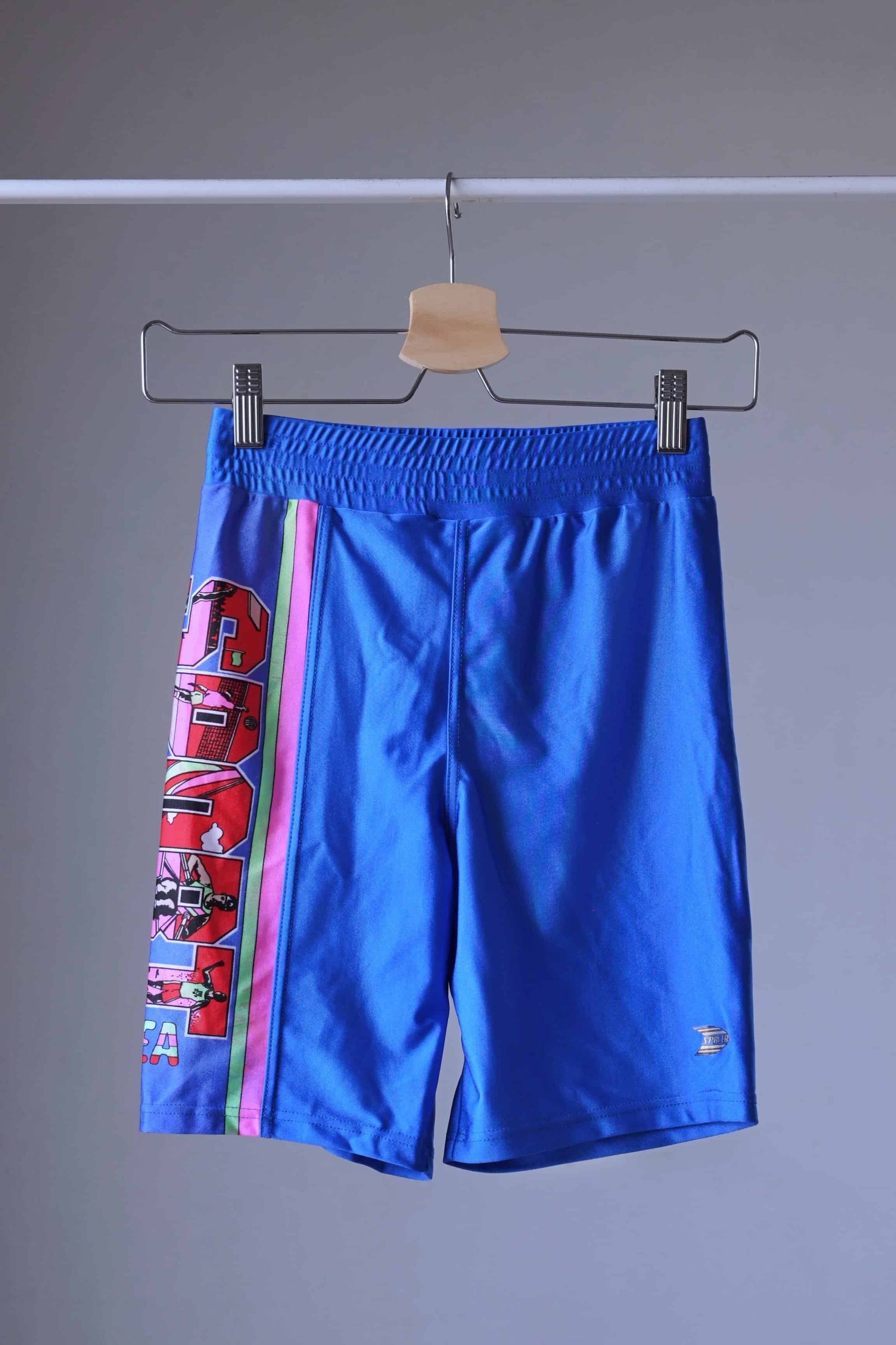 Front view of the blue vintage Sprider swim trunks hanging on a hanger.