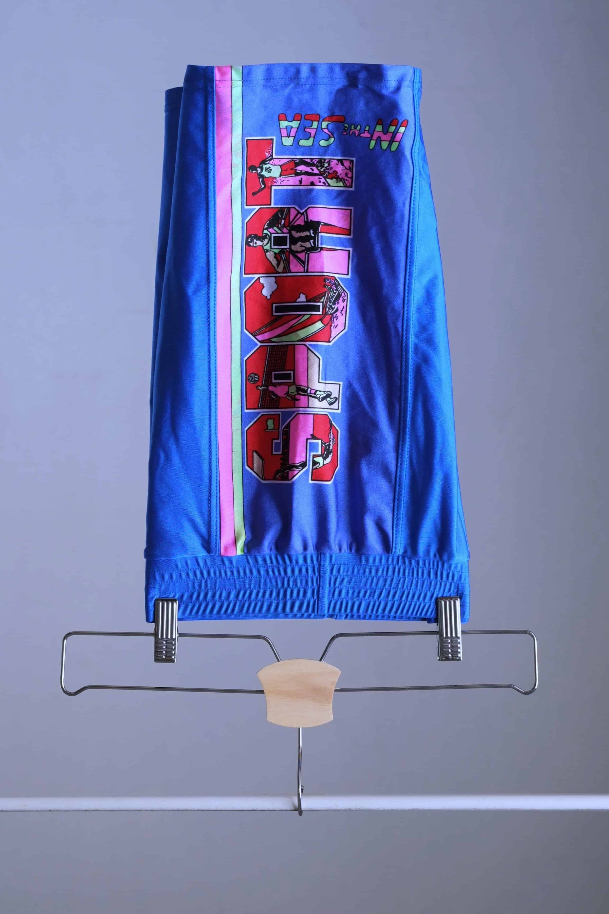 Side view of the blue vintage Sprider swim trunks hanging on a hanger.