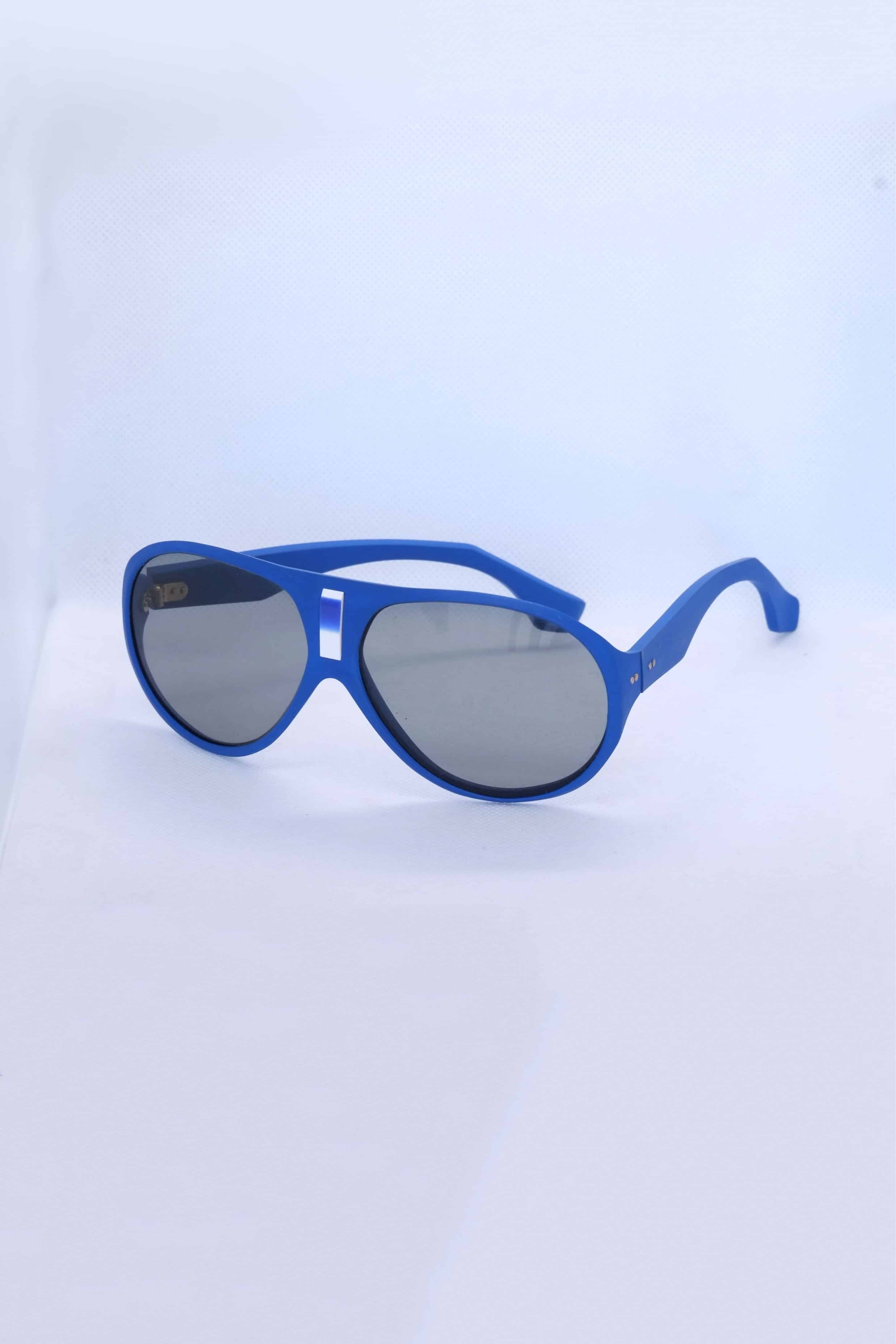 Angled view of vintage 1970s SKILOOK matte cobalt blue shield-style alpine sunglasses with a silver metallic nose bridge accent and gray lenses against a white backdrop.