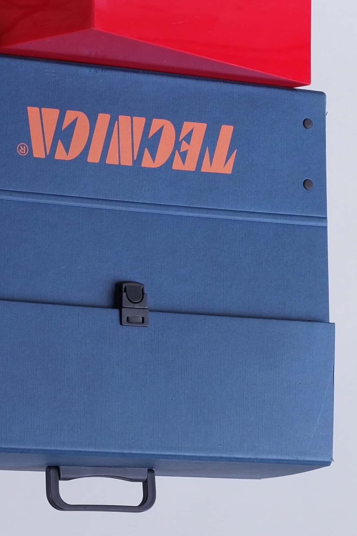 Detail shot showing corner of the Tecnica case with rivets and part of the orange logo.