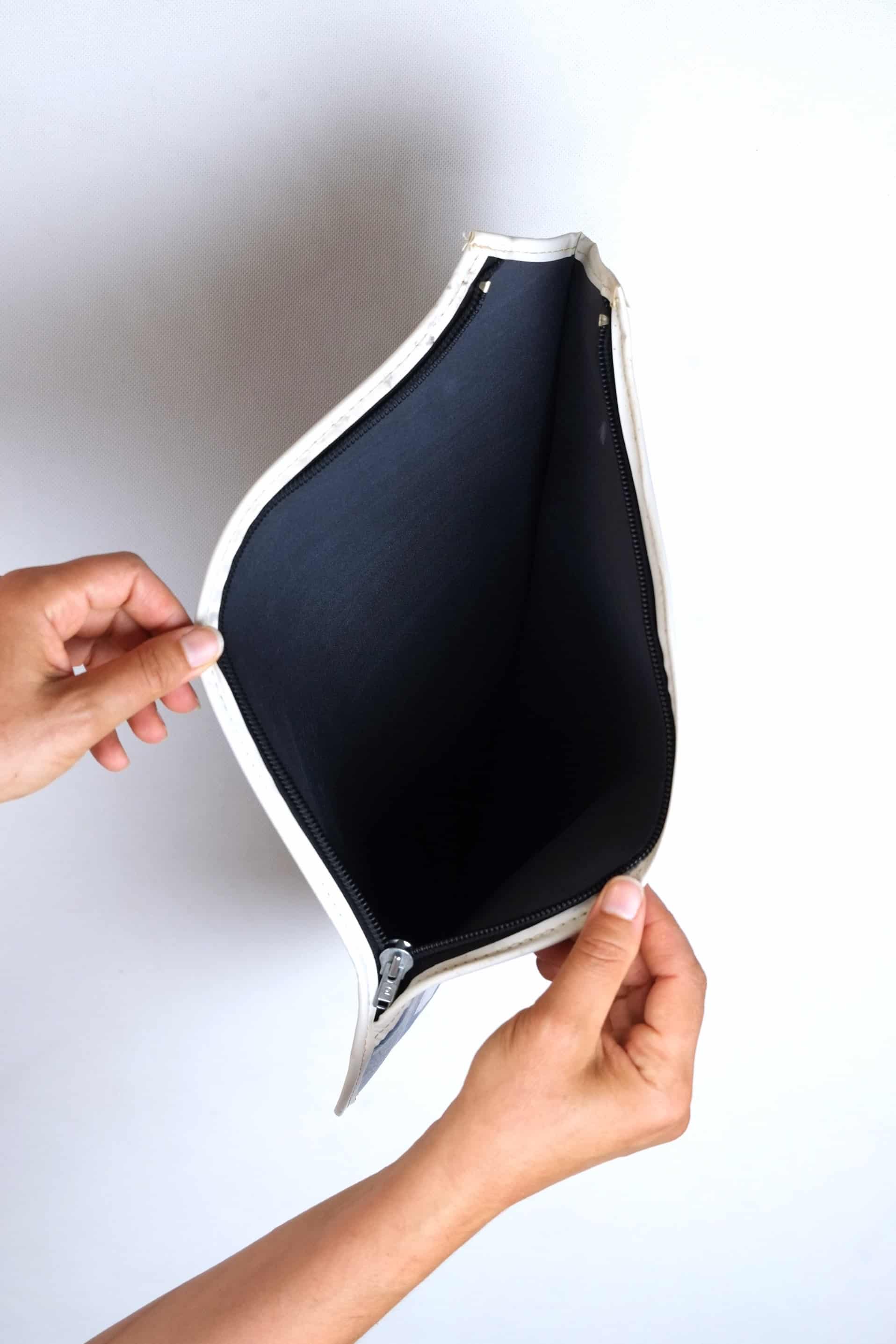 Hands pulling open a vintage white vinyl Tretorn tennis racket cover, showcasing the clean, dark blue fabric interior lining and black zipper track.