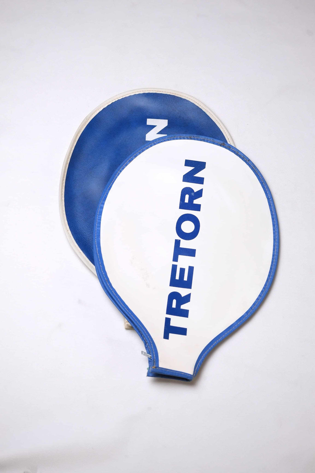 Two vintage Tretorn vinyl tennis racket covers stacked together: a top white cover with blue trim and vertical text, and a bottom blue cover with white trim.