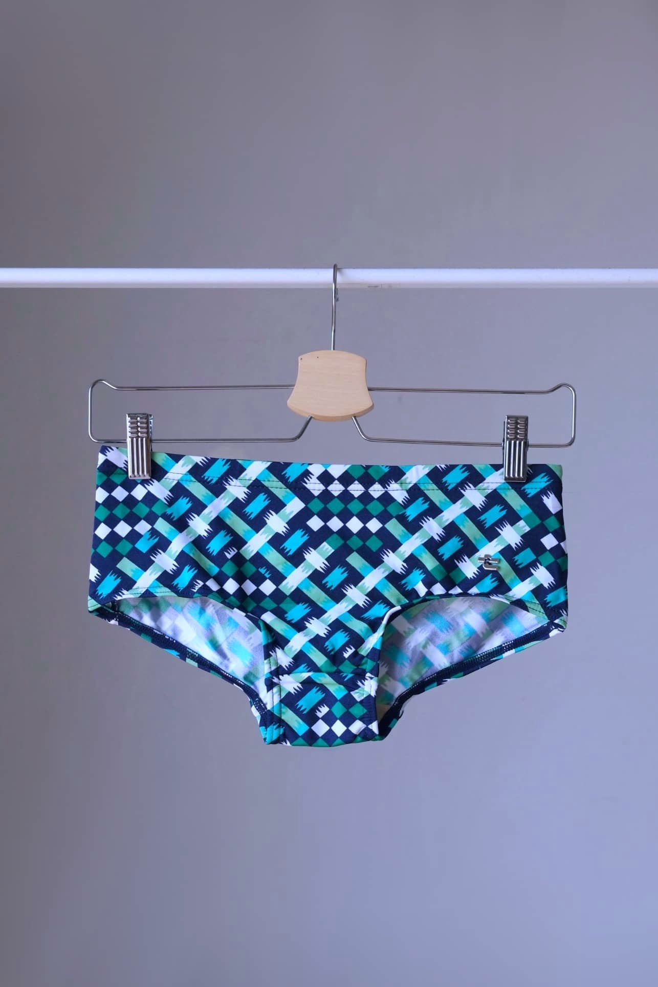 swim briefs in a geometric pattern of blue,  green and white on a hanger