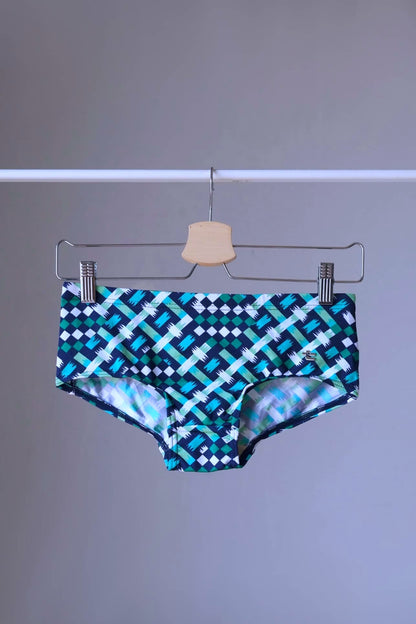 swim briefs in a geometric pattern of blue,  green and white on a hanger